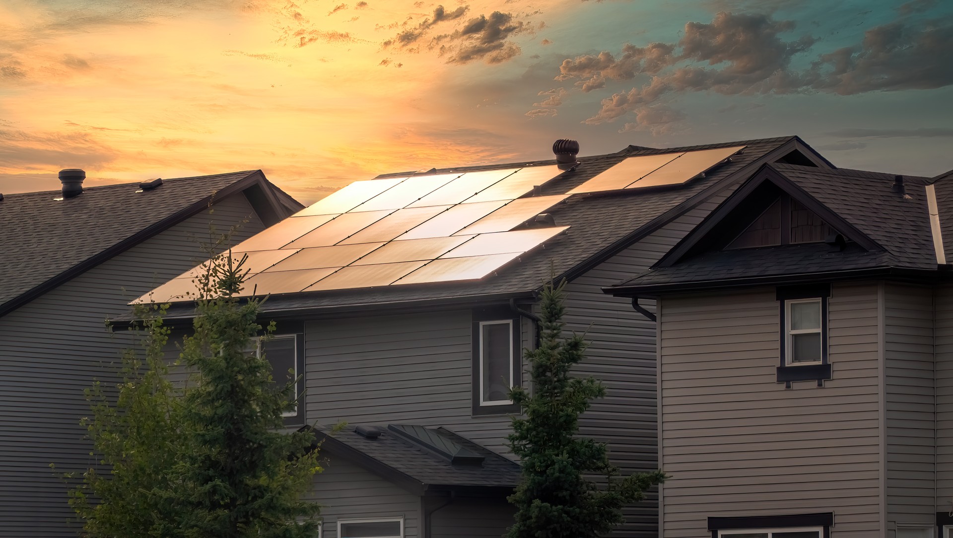 A residential home with a solar panel installation on the roof, capturing the setting sun against a vibrant sky.